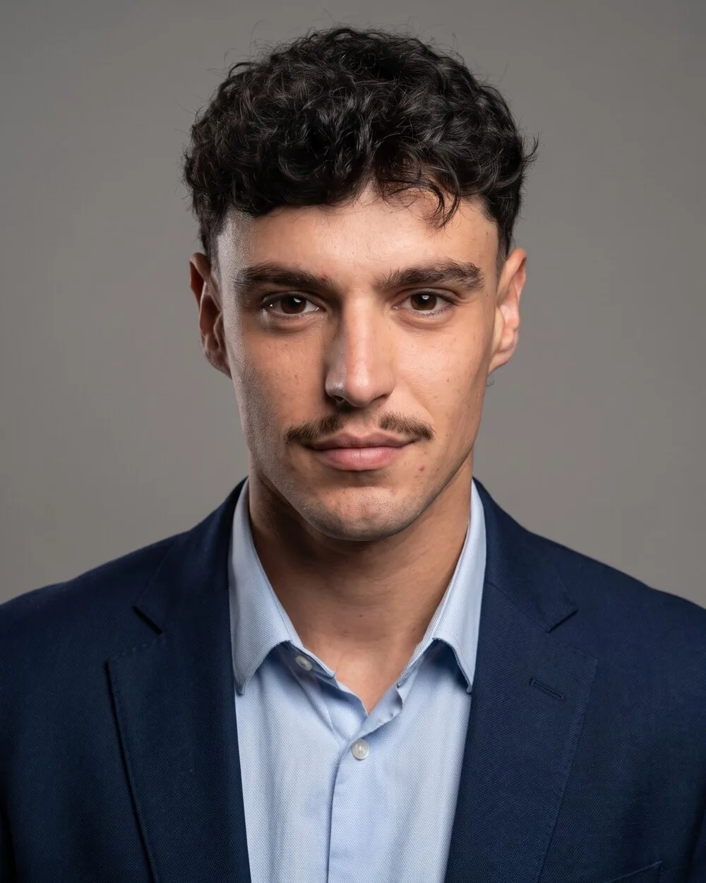 Portrait of Diogo Frias in a navy blazer and light blue shirt against a grey background